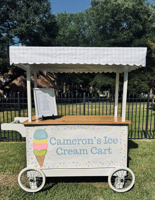 Ice cream cart with 'Cameron's Ice Cream Cart' sign on a grassy area